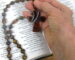 Hand holding Protestant prayer beads over open Bible during prayer