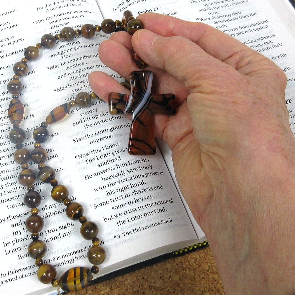 Hand holding Protestant prayer beads over open Bible during prayer