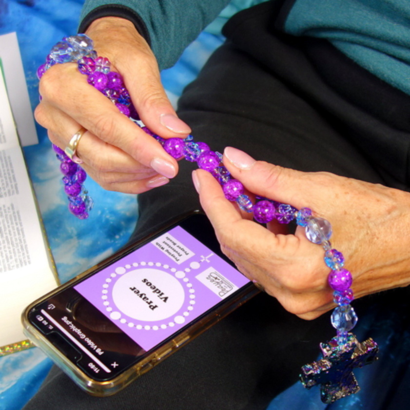 Woman's hands holding Protestant prayer beads above phone showing guided prayer video.