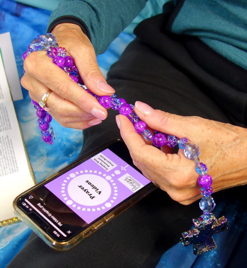 Hands holding prayer beads over phone showing prayer video image